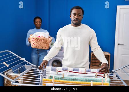Junge afroamerikanische Paar hängende Kleidung an Wäscheleine Denken Haltung und nüchternen Ausdruck selbstbewusst aussehen Stockfoto