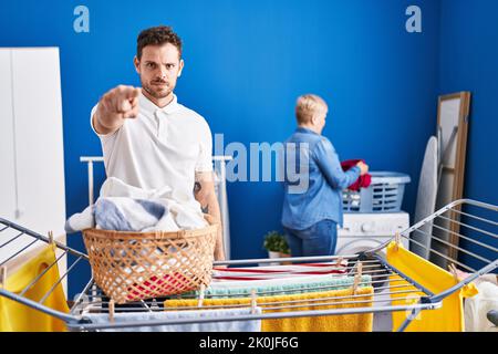 Hispanische Mutter und Sohn hängen Kleidung an der Wäscheleine, zeigen mit dem Finger auf die Kamera und auf Sie, selbstbewusste Geste, die ernst aussieht Stockfoto