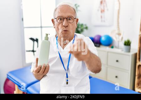 Leitender Physiotherapie-Mann hält Massage Körperlotion mit dem Finger auf die Kamera und auf Sie, selbstbewusste Geste, die ernst aussieht Stockfoto