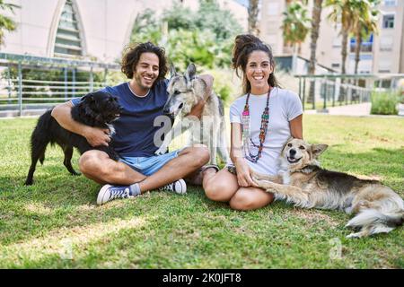 Mann und Frau Paar lächeln selbstbewusst auf Kraut mit Hunden im Park sitzen Stockfoto