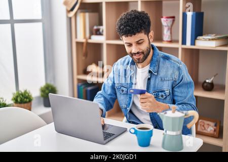 Junger arabischer Mann mit Laptop und Kreditkarte, der zu Hause auf dem Tisch sitzt Stockfoto