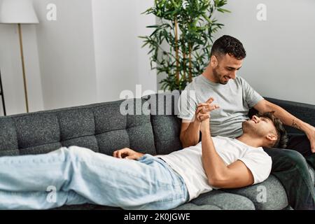 Zwei hispanische Männer, die zu Hause lächeln und selbstbewusst auf dem Sofa sitzen Stockfoto