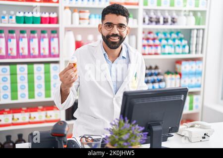 Junger arabischer Mann Apotheker mit Computer hält Pillen Flasche in der Apotheke Stockfoto