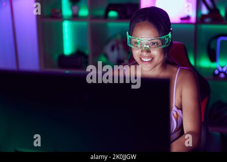 Junge hispanische Frau streamer mit Computer und Virtual-Reality-Brille im Spielzimmer Stockfoto