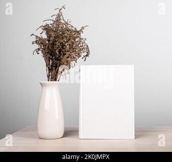 Buch Mockup und getrockneten Blumen Bouquet in Vase an Holztisch. Schönes und zartes Interieur des Leseliebhabers in minimalistischem Stil. Roman mit leerem CO Stockfoto