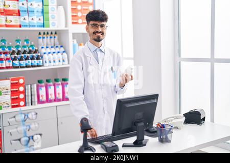 Junger hispanic Mann Apotheker hält Pillen Flasche mit Computer in der Apotheke Stockfoto