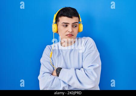 Nicht-binäre Person, die mit Kopfhörern Musik hört, die zur Seite schauen und die Arme überkreuzt haben, überzeugt und selbstbewusst Stockfoto