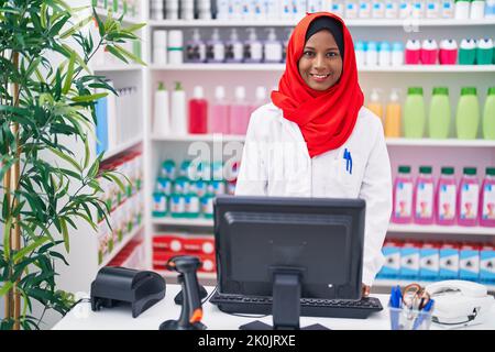 Junge schöne Frau Apotheker lächelt zuversichtlich mit Computer in der Apotheke Stockfoto