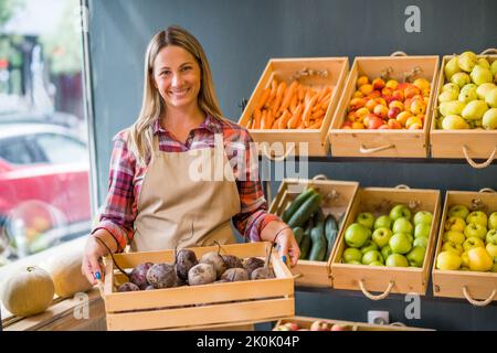 Frau arbeitet im Obst- und Gemüseladen. Sie hält einen Korb mit Rote Bete. Stockfoto