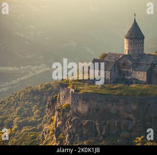 Altes vintage Kloster, Berg Hügel in Sonnenuntergang. Tatev antikes Kloster in sanftem orangefarbenem Licht. Armeniens berühmteste Reisestelle. Beliebtes Touristenziel. Alte mittelalterliche Architektur. Reisetourismus Stockfoto