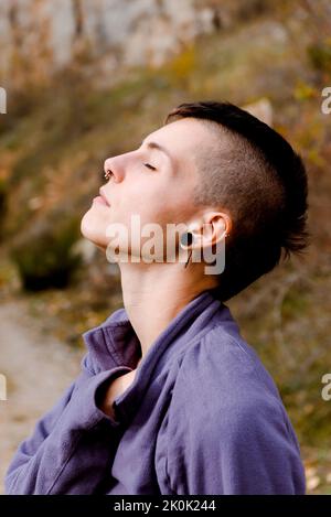 Seitenansicht einer ruhigen jungen Dame in legerer Kleidung mit geschlossenen Augen, die frische Luft atmet und durch den herbstlichen Wald reist Stockfoto