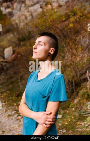 Seitenansicht einer ruhigen jungen Dame in legerer Kleidung mit geschlossenen Augen, die frische Luft atmet und durch den herbstlichen Wald reist Stockfoto