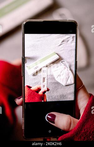 Von oben der Ernte anonyme Frau, die Foto von schnellen Antigen-Test und medizinische Maske auf dem Smartphone während der Coronavirus-Pandemie auf verschwommenem Backgroun Stockfoto