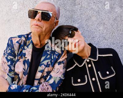 Älterer Mann in modischem Outfit und fröhliche Frau in schwarzem Kleid, die in der Nähe der Mauer in der Stadt steht Stockfoto