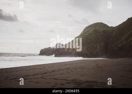 Winkende, vom Meer spülende Sandküste mit Wanderwegen und raue, felsige Berge, die mit Gras bedeckt sind, gegen den bewölkten Himmel in der wilden Natur Stockfoto