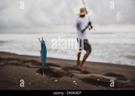 Soft Focus Rückansicht ganzer Körper von anonymen Fischern, die Angelrute mit Stöpsel schwingen, während sie an der Küste in der Nähe des winkenden Meeres stehen Stockfoto