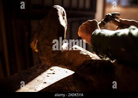 Leitender Holzarbeiter in Gläsern mit Meißel und Hammer, während er in der Werkstatt mit einem Stück Holz arbeitet Stockfoto