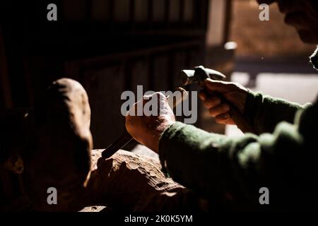 Leitender Holzarbeiter in Gläsern mit Meißel und Hammer, während er in der Werkstatt mit einem Stück Holz arbeitet Stockfoto