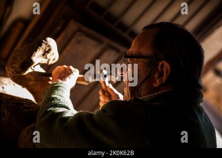 Leitender Holzarbeiter in Gläsern mit Meißel und Hammer, während er in der Werkstatt mit einem Stück Holz arbeitet Stockfoto