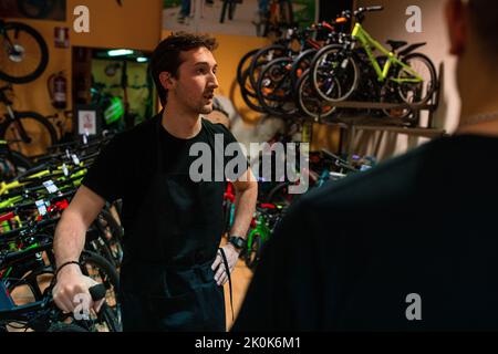 Junge Kassiererin in schwarzem T-Shirt lächelnd und mit Computern, während sie im modernen Fahrradladen arbeitete Stockfoto