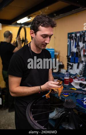 Junger Mann im Vorfeld pumpt Luft in Fahrradreifen, während er in einer professionellen Werkstatt arbeitet Stockfoto