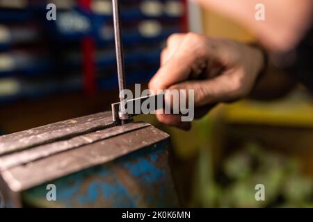 Unerkennbarer Handwerker, der dünne Metallstäbchen mit Feile schleifend, während er in der professionellen Garage arbeitet Stockfoto
