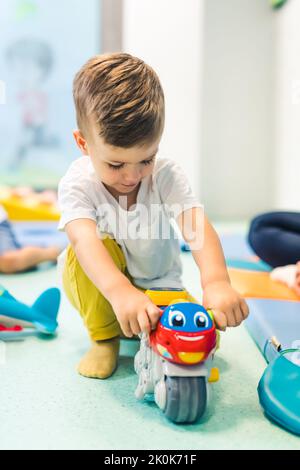 Vorstellungskraft und kreative Denkentwicklung. Sprach- und Sozialkompetenz. Kleinkind spielt mit bunten Plastikspielzeug und bunten Auto in einem Kindergarten Spielzimmer. Hochwertige Fotos Stockfoto