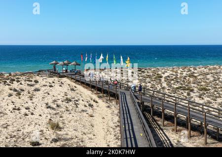 Touristen, die auf dem Holzsteg zum Strand und über das Naturschutzgebiet Parque Natural da Ria Formosa in der Nähe von Quinta do Lago gehen Stockfoto