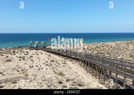 Touristen, die auf dem Holzsteg zum Strand und über das Naturschutzgebiet Parque Natural da Ria Formosa in der Nähe von Quinta do Lago gehen Stockfoto