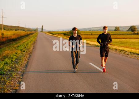 Junge Freunde, die auf der Straße sprinten. Fit Runner Fitness Runner während Outdoor-Training mit Sonnenuntergang Hintergrund Stockfoto