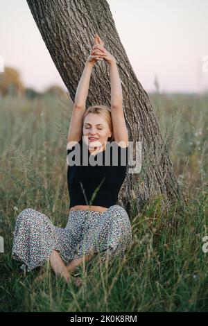 Unter einer baumblonden Frau auf Gras sitzend Stockfoto