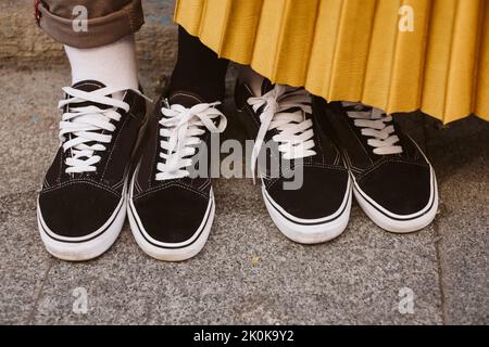 Blick von oben auf ein anonymes Paar Füße in schwarzen Sneakers und weißen Schnürsenkeln, während sie auf der Straße stehen Stockfoto