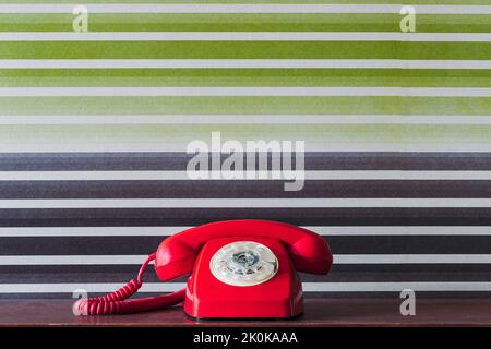 Rotes Telefon im Retro-Stil mit Hörer auf Holztisch vor bunt grün und lila gestreiftem Hintergrund platziert Stockfoto