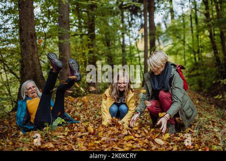 Happy Little girl with mother and Großmutter having fun with blätters during herbsting walk in Stockfoto