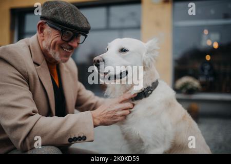 Glücklicher älterer Mann, der seinen Hund während eines Spaziergangs im Freien in der Stadt mit Halsband gab. Stockfoto