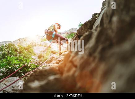 Aktive Klettererin mit Schutzhelm Abseilen von der Felswand mit Seil mit Sicherungsvorrichtung und Klettergurt. Aktive Extremsportzeit Stockfoto