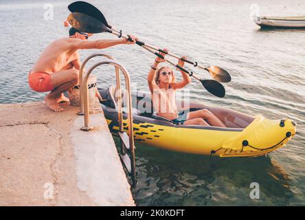 Vater mit Teenager Sohn Vorbereitung Abendfahrt Laden Ruder in einem aufblasbaren Kajak. Adriaküste Hafen in Kroatien in der Nähe von Sibenik Stadt. Urlaub A Stockfoto