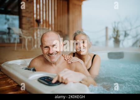 Ältere Paare genießen gemeinsam eine Badewanne im Freien auf ihrer Terrasse während des kalten Wintertages. Stockfoto