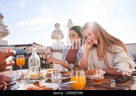 Glückliche junge Freundinnen essen leckere Pizza und plaudern, während sie sich auf der Terrasse am sonnigen Sommertag treffen Stockfoto
