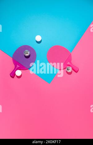 Partyhintergrund mit zwei Tischtennisschlägern mit zwei weißen Tischtennisbällen und zwei glänzenden Disco-Bällen. Stockfoto