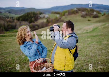 Glücklicher junger Mann mit Down-Syndrom mit seiner Mutter, die in der Natur ruhte, mit einem Fernglas saß und schaute. Stockfoto