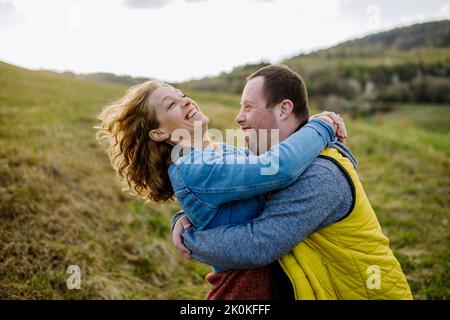 Outdoor-Porträt der Mutter umarmt ihren erwachsenen Sohn mit Down-Syndrom, Mutterschaft Konzept. Stockfoto