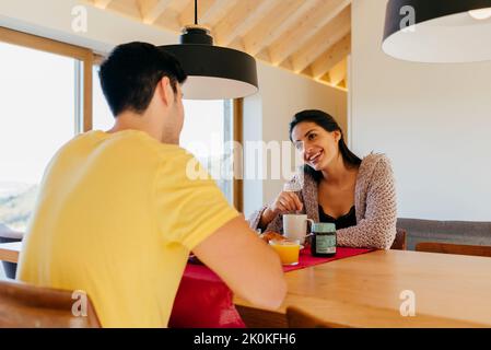 Attraktive hispanische glückliche Dame und junger Mann beim gemeinsamen Frühstück am Tisch in der modernen Küche Stockfoto