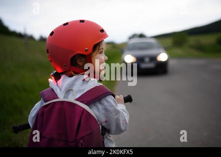 Rückansicht eines Kindes, das Fahrrad auf der Straße fährt, mit einem Auto vor ihr, Konzept zur Aufklärung der Verkehrssicherheit. Stockfoto