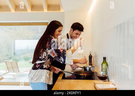 Seitenansicht der attraktiven hispanischen jungen Dame und des jungen Mannes, die in der Küche zusammen kochen Stockfoto