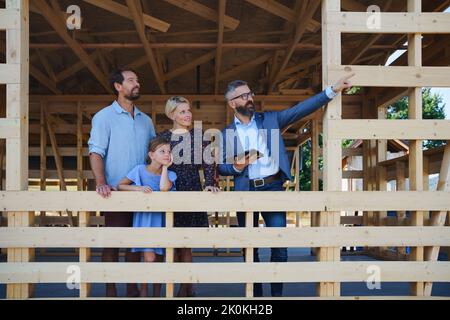 Vertriebsmitarbeiter zeigt jungen Familien auf der Baustelle Pläne für ein neues Haus. Stockfoto