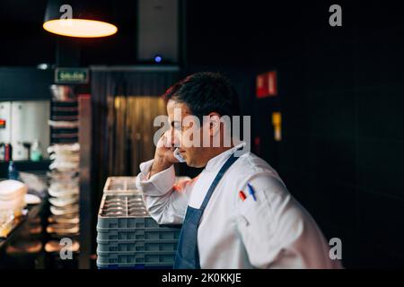 Seitenansicht des Mannes, der in der Restaurantküche arbeitet und einen Anruf hat Stockfoto