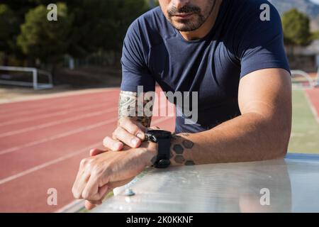 Crop unkenntlich männlichen Läufer Vorbereitung seiner Smart-Uhr während des Trainings im Stadion an sonnigen Tag Stockfoto