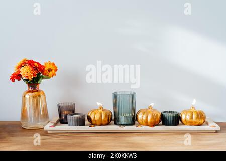 Herbst, Herbst gemütliche Zusammensetzung. Frische Dahlia-Blumen in Vase und Kürbis-förmige goldene Kerzen auf dem Holztablett mit weißem Wandhintergrund. Skandinavien Stockfoto