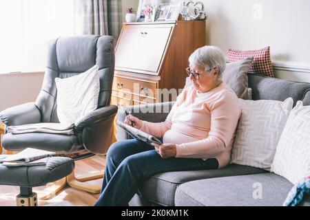 Alte ältere Frau, 80s Erwachsene, Großmutter, die Kreuzworträtsel in ihrem Wohnzimmer macht, das auf dem Sofa sitzt. Ruhestandhobby für Trainingsgedächtnis. Alzhe Stockfoto